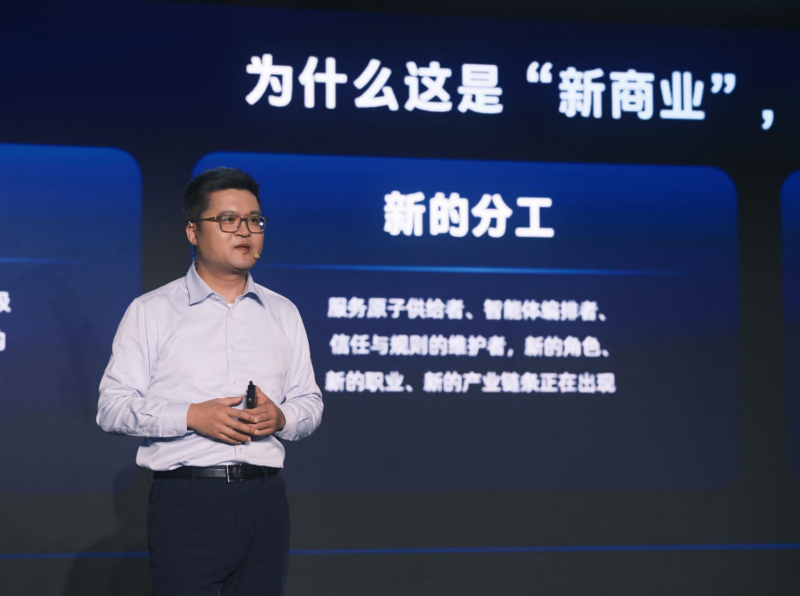 支付宝AI生态大会会场，演讲者身后大屏写着「为什么这是新商业」「新的分工」