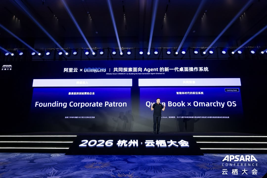 2026 云栖大会现场，大屏展示“阿里云 × OMARCHY：共同探索面向 Agent 的新一代桌面操作系统”，左栏为“Founding Corporate Patron”，右栏为“Qwen Book × Omarchy OS”