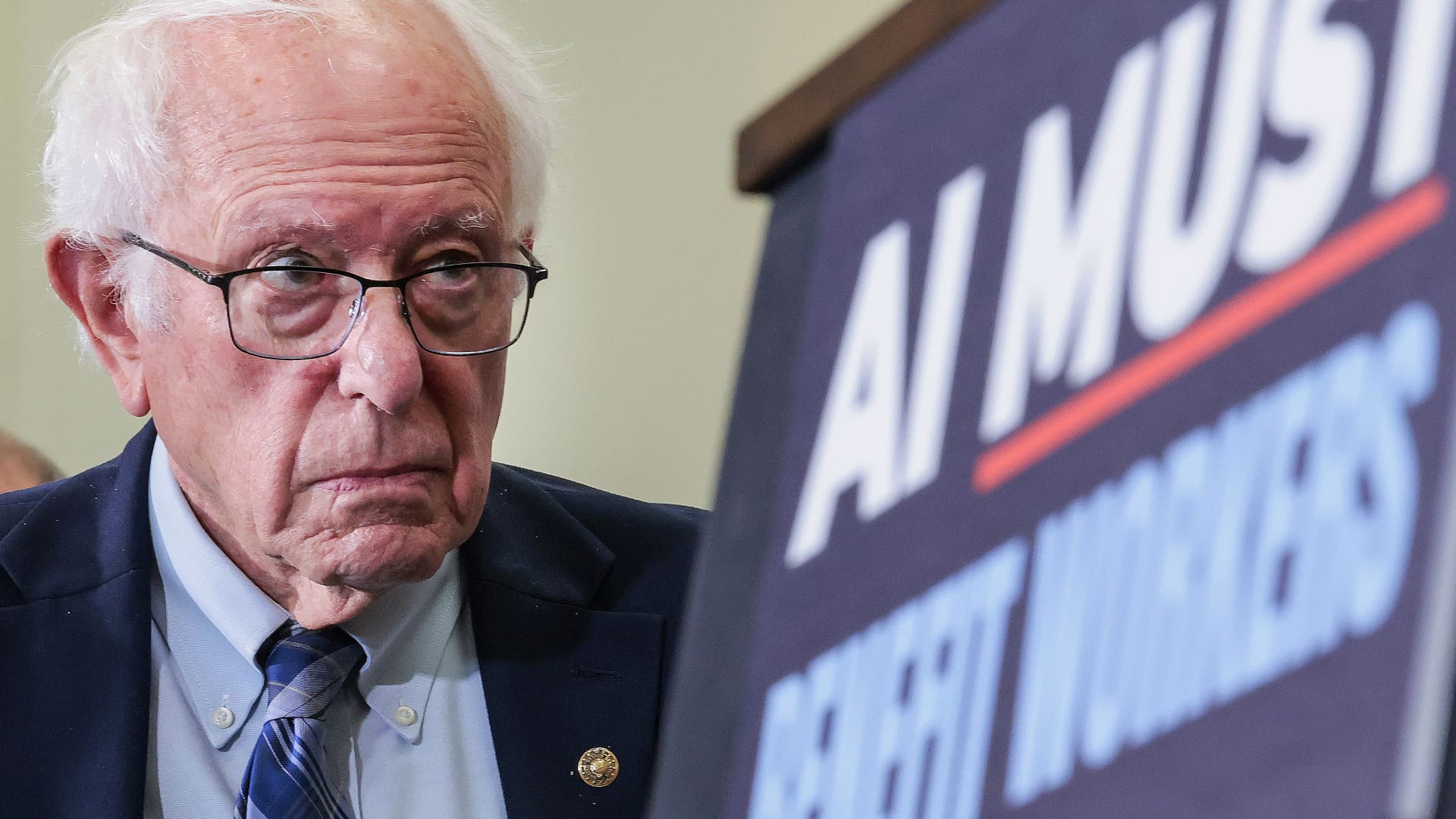 参议员 Bernie Sanders 与写有「AI MUST」的标语牌