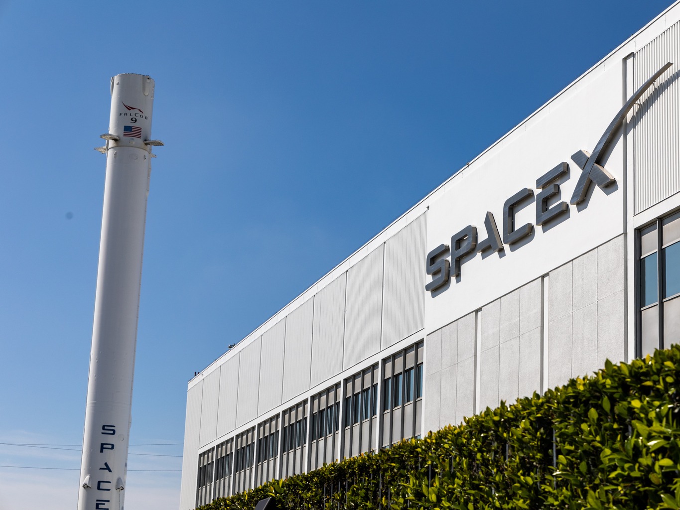 SpaceX 位于加州霍桑的总部，建筑外立面上有 SpaceX 标志，左侧竖立着一枚猎鹰 9 号火箭