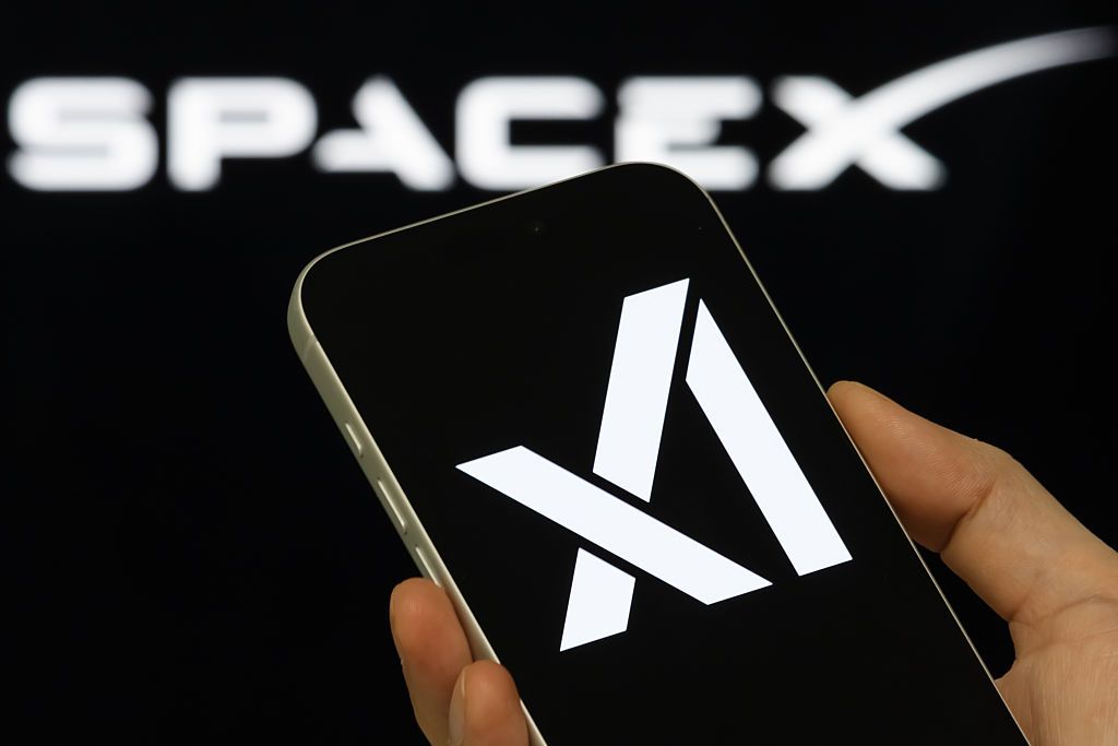 手机屏幕上显示 xAI 标识，背景为 SpaceX 字样（TechCrunch 报道配图，Getty Images）