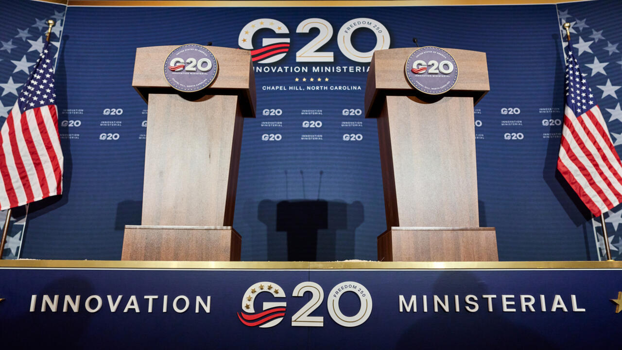 G20 创新部长级会议设在教堂山的主会场：蓝色背景板印有会议名称与 Chapel Hill, North Carolina 字样，台前是两支讲台话筒和美国国旗（图源 Matt Ramey / AFP）