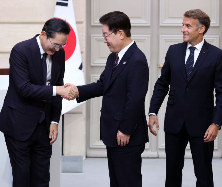 投资协议仪式结束后，韩国总统李在明与三星会长李在镕握手，法国总统马克龙在旁（韩联社图说）