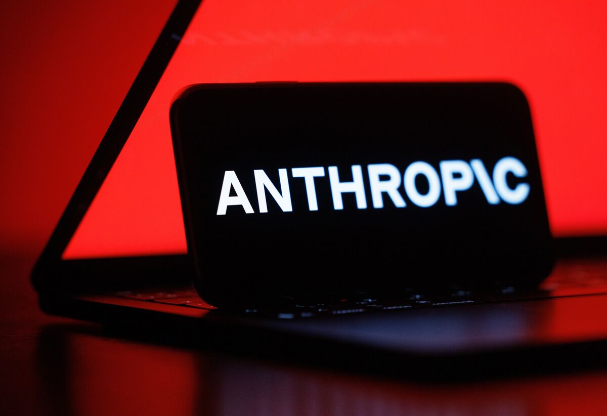 红色背光下，一部手机屏幕显示 Anthropic 标志（彭博报道配图）