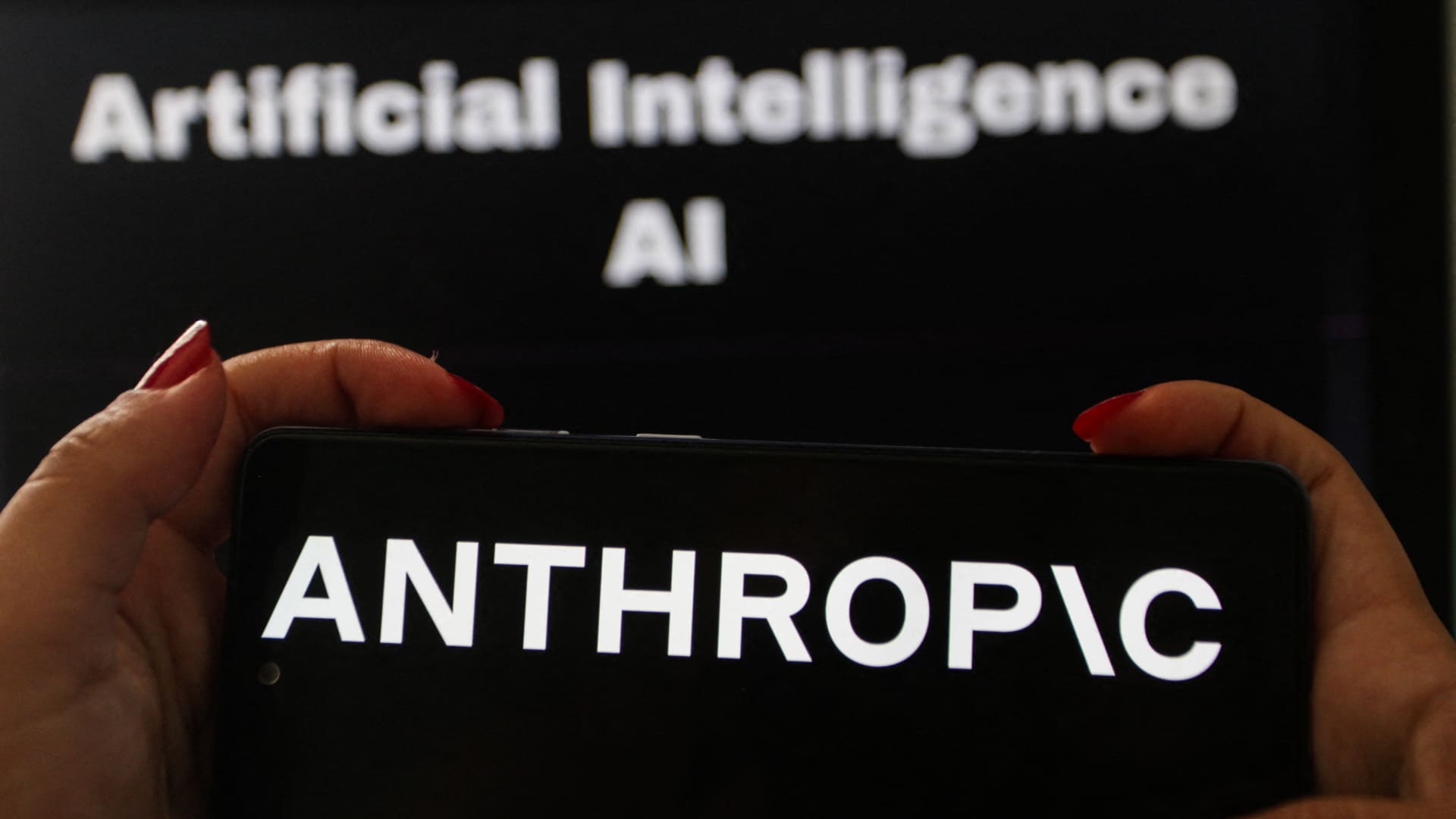 有人手持一部屏幕显示 Anthropic 标志的手机，背景屏幕写着 Artificial Intelligence