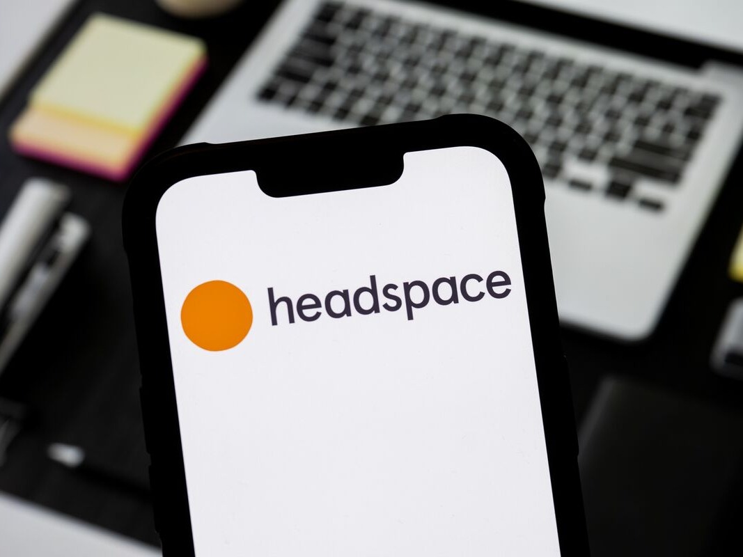 一部智能手机的屏幕上显示 Headspace 应用标识，背景是办公桌与笔记本电脑
